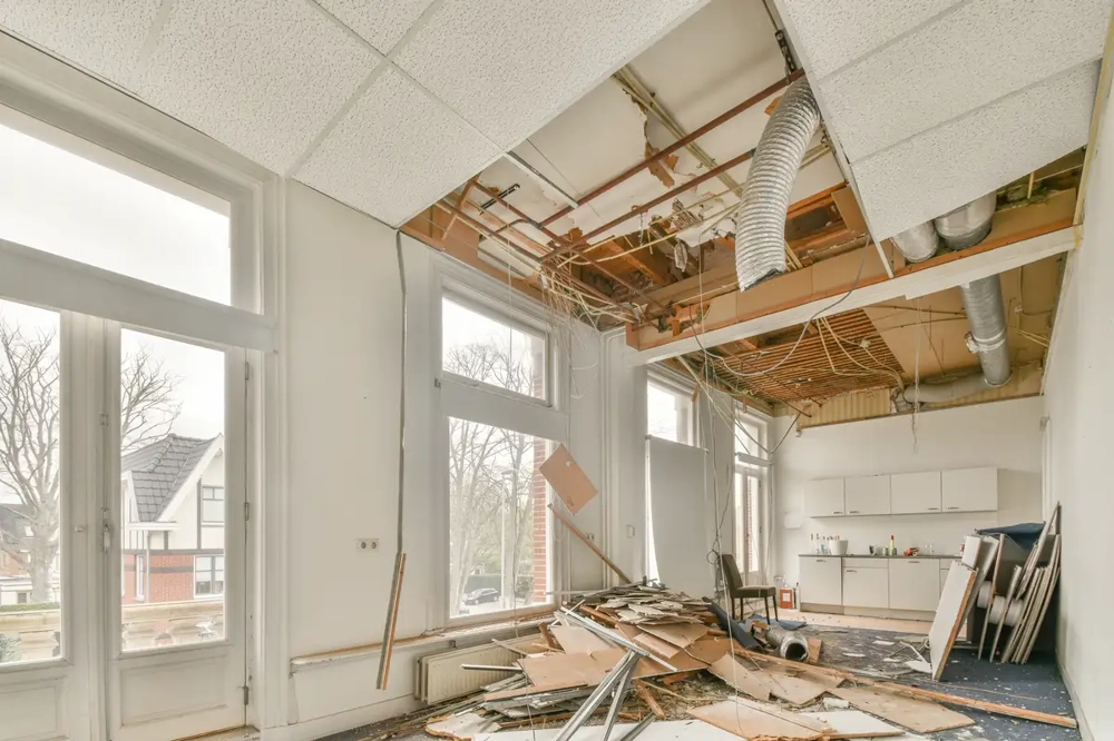 Offene Deckenstruktur, freigelegte Leitungen und Bauschutt auf Boden bei Abrissarbeiten in Innenraum