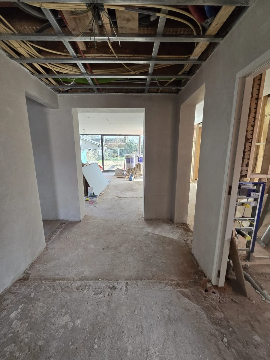Flur mit abgehängter Decke und Sichtleitungen, verputzten Wänden und vorbereitetem Boden (Trockenbau)