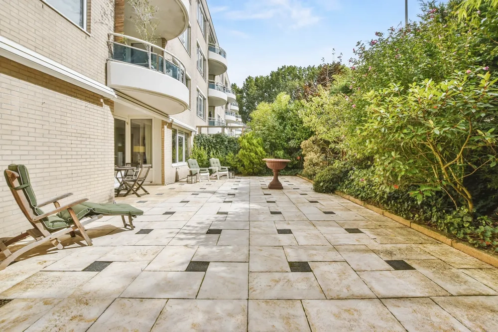 Terrassenbau mit großformatigen hellen Steinplatten, Gartenrandbegrünung und Sitzmöbeln vor Wohngebäude