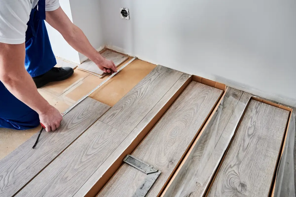 Handwerker beim Laminat verlegen misst mit Zollstock den Untergrund und fügt graue Holzoptik-Paneele an der Wand ein